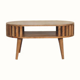 A medium-sized round coffee table made of natural finish mango wood, featuring a slatted design and an open shelf.