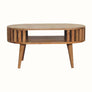 A medium-sized round coffee table made of natural finish mango wood, featuring a slatted design and an open shelf.