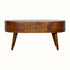 A round, chestnut finish mango wood coffee table with four tapered legs and two drawers with brass knob hardware.