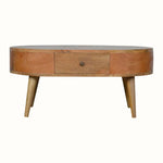 A round, natural finish mango wood coffee table with four tapered legs, featuring two drawers with brass knob hardware.