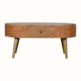 A round, natural finish mango wood coffee table with four tapered legs, featuring two drawers with brass knob hardware.