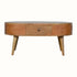 A round, natural finish mango wood coffee table with four tapered legs, featuring two drawers with brass knob hardware.