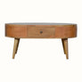 A round, natural finish mango wood coffee table with four tapered legs, featuring two drawers with brass knob hardware.