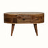 A small round natural-colored coffee table made of mango wood, with four tapered legs and two drawers with brass knob hardware.