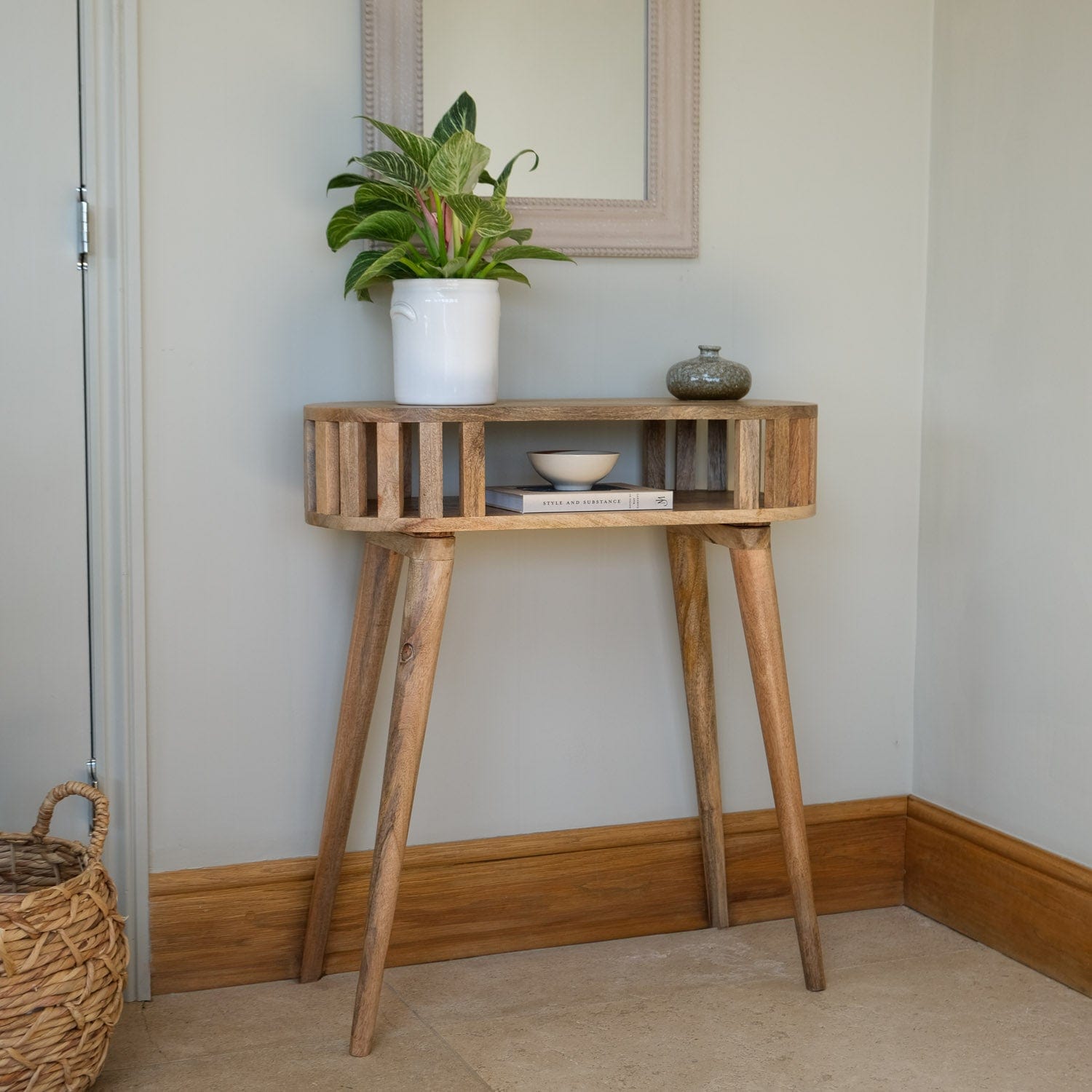 Wooden side table with a plant and decorative items against a neutral wall.