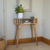 Wooden side table with a plant and decorative items against a neutral wall.