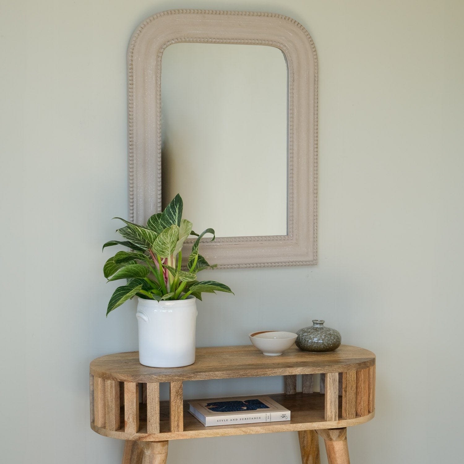 Wooden console table with a plant, books, and decorative items against a light wall.