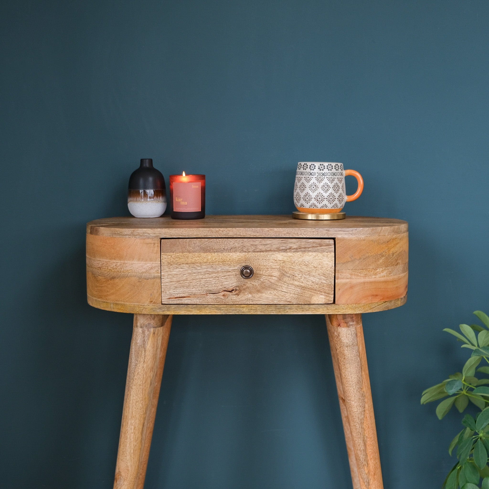 A curved-shaped, natural finish console table with a drawer and tapered legs, made from solid mango wood.