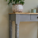 Wooden table with a plant and a small container on a neutral background