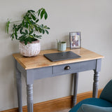 Small wooden table with a plant, tablet, and photo frame against a plain wall.